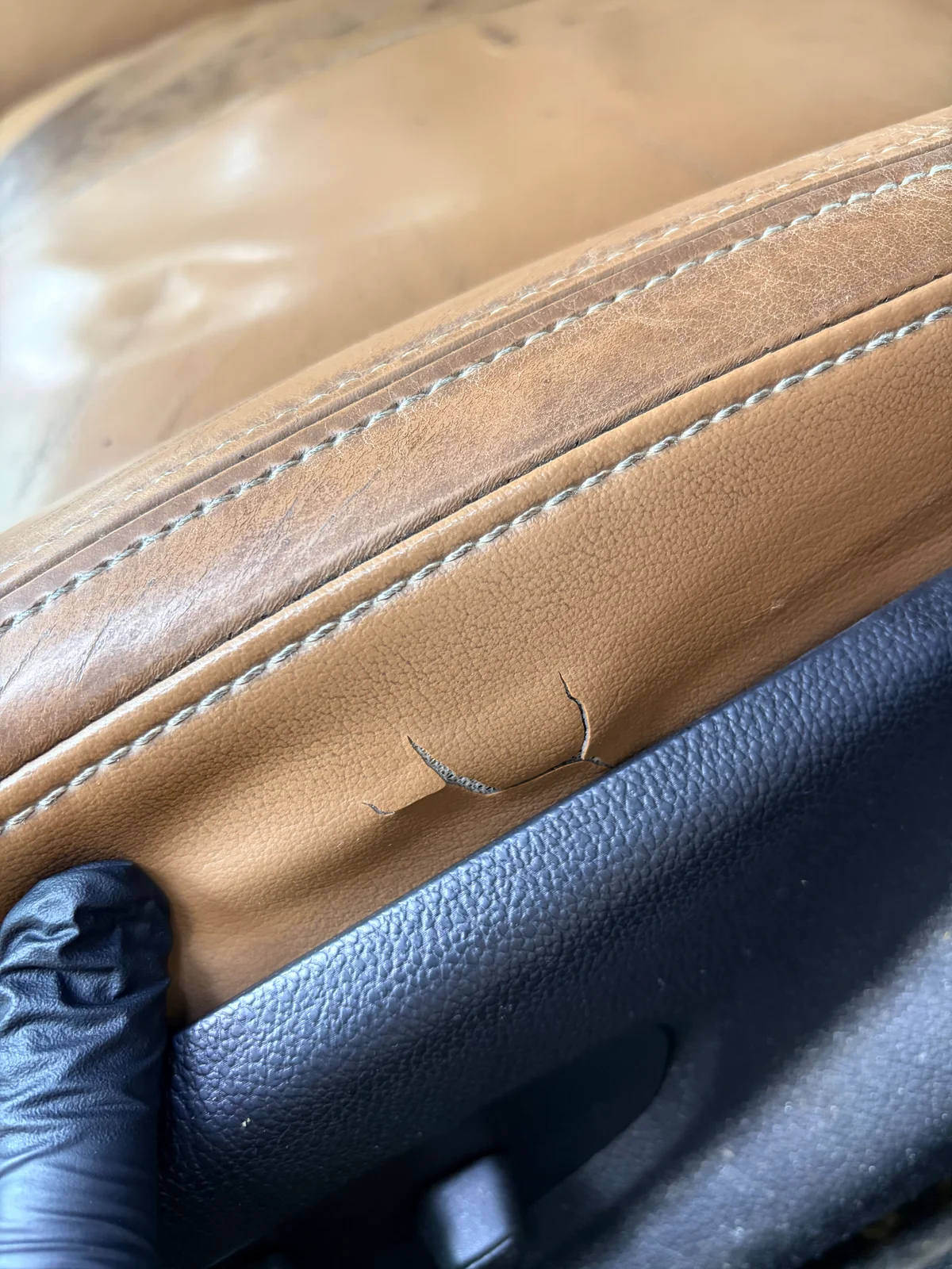 2015 Buick LaCrosse lower vinyl side panel before restoration — tear near the seat's lower trim, distinct from the leather seating surface