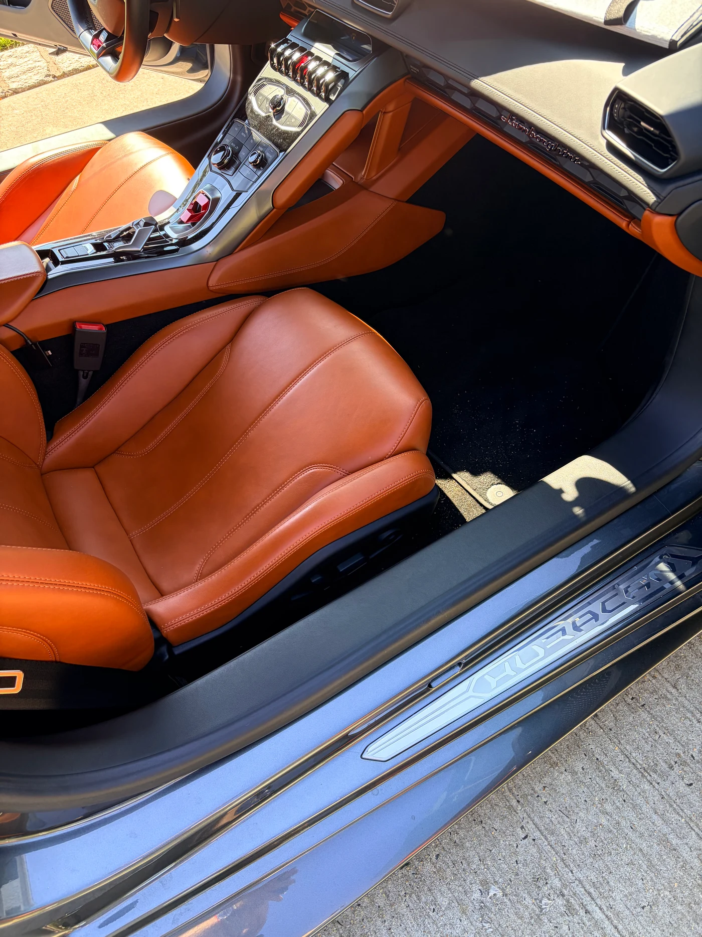 Lamborghini Huracán cabin overview — orange leather seat, Huracán-branded door sill, and passenger footwell