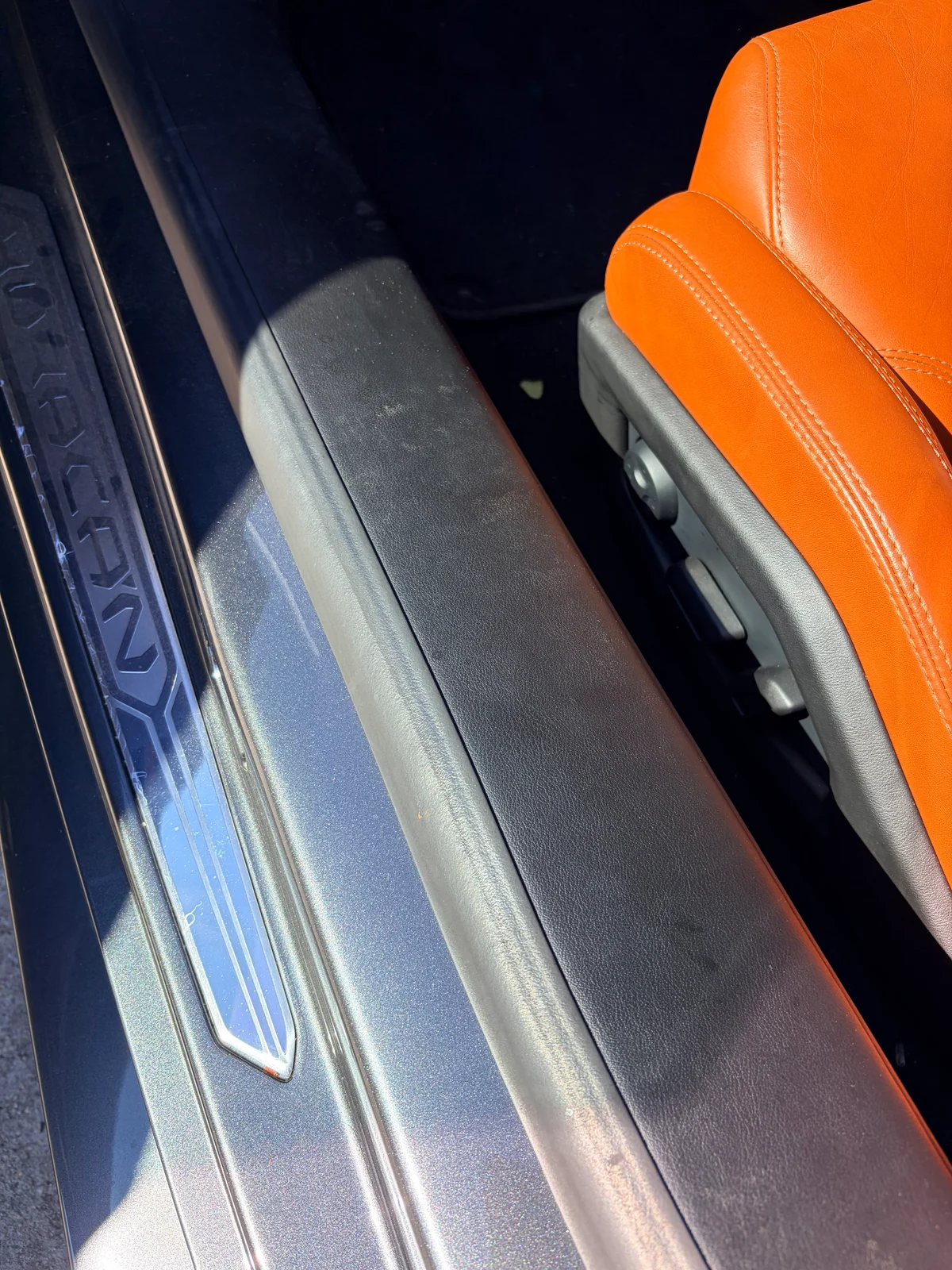 Lamborghini Huracán leather entry panel before restoration — surface scuffing beside the driver's seat, next to the Huracán-branded door sill plate