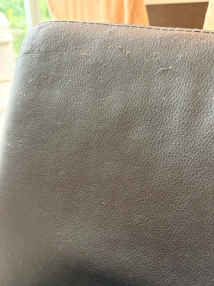 Close view of numerous cat-claw scratches on a black leather chair back before restoration