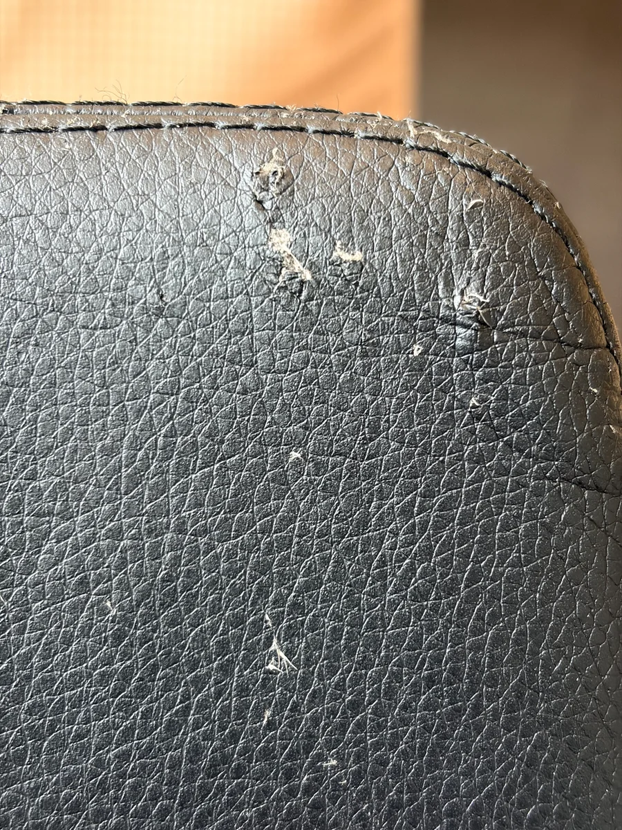 Detail of deeper cat-claw marks near the stitched edge of a black leather chair before repair