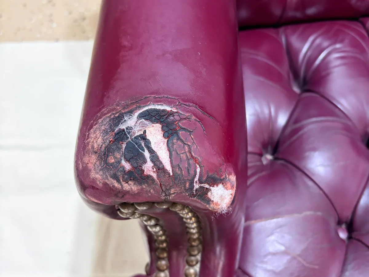 Chesterfield chair armrest before restoration — leather worn through to substrate, large hole visible