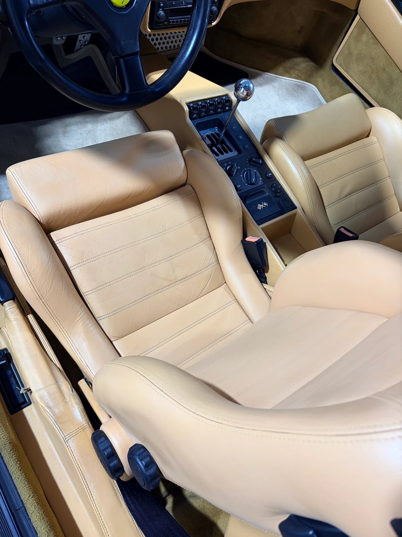 Ferrari F355 Berlinetta cabin after restoration — steering wheel, open-gate shifter, and both tan leather seats showing consistent, naturally integrated finish