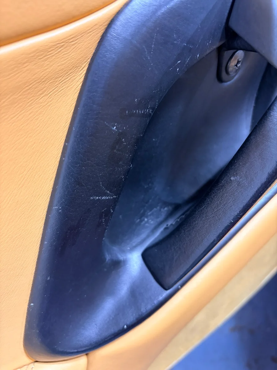 Ferrari F355 door card before restoration — fine surface scratches across the leather-wrapped interior handle surround
