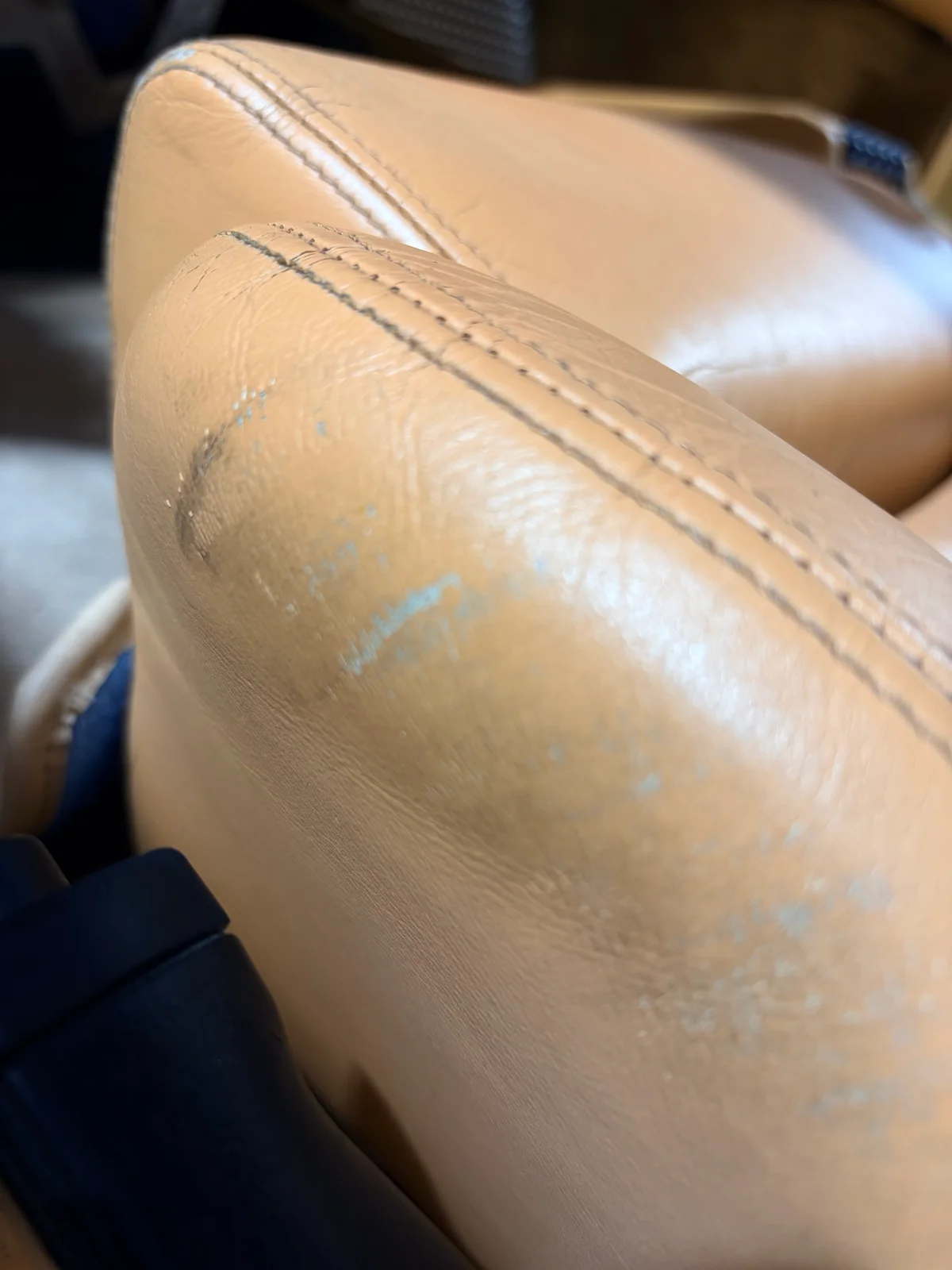 Ferrari F355 driver's seat bolster before restoration — surface cracking and denim discoloration concentrated on the lower bolster edge