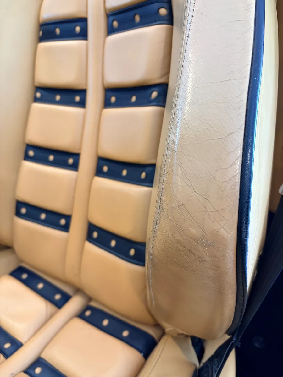 Ferrari F430 seat bolster junction before restoration — dealership overspray and color mismatch visible against original Cuoio leather