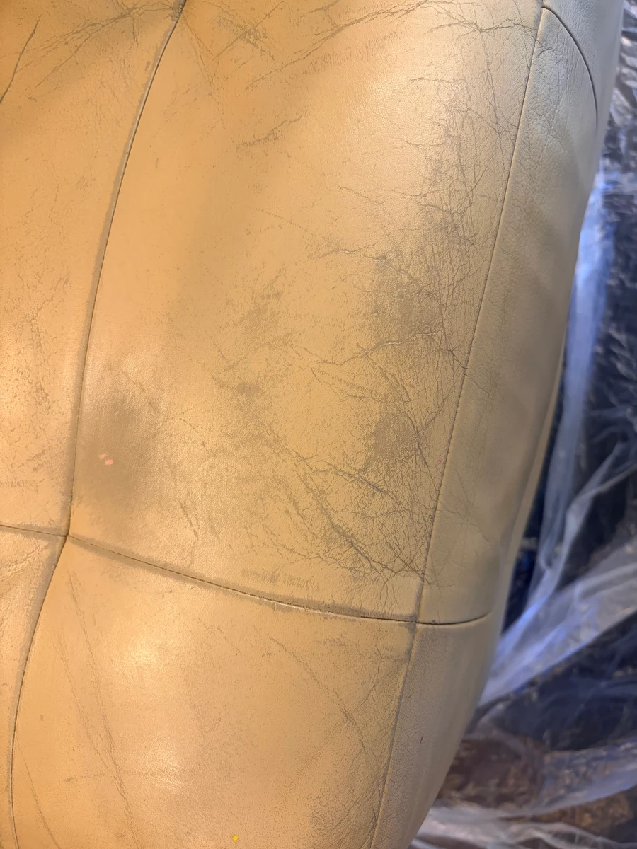 Cream leather banquette backrest before restoration — fine surface crazing across the tufted panel visible in raking light