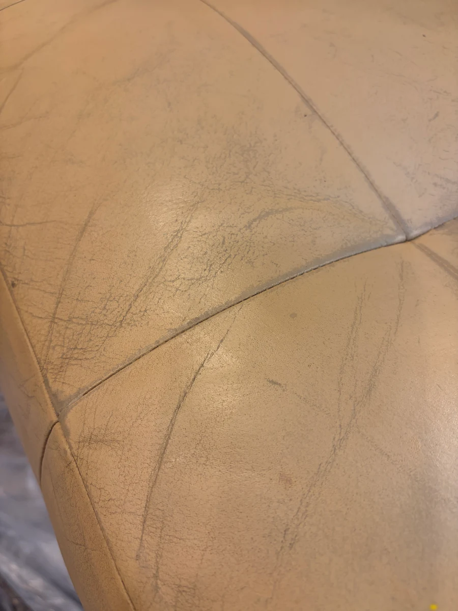 Close-up of cream leather banquette seat showing surface crack network before restoration — finish failure from drying and repeated flexion