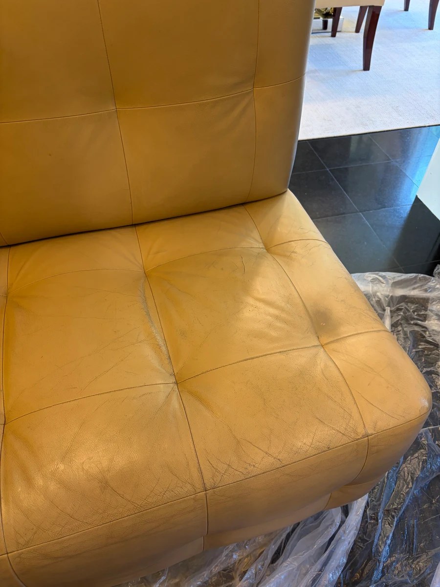 Single cream leather banquette seat section before restoration — yellowing, surface cracking, and finish wear visible across the tufted seat cushion