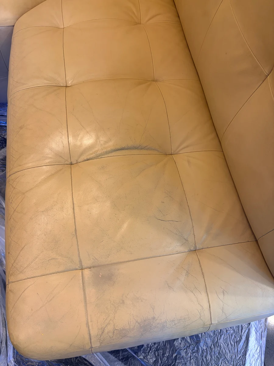 Cream leather kitchen banquette seat surface before restoration — widespread surface cracking and yellowing visible across the tufted panels