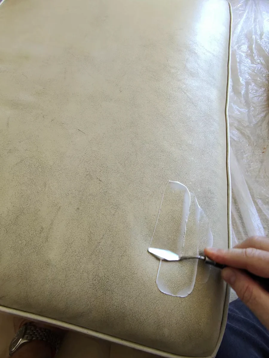 Professional leather crack filler applied by hand with palette knife to sofa cushion surface — restoration process during furniture color restoration in New York