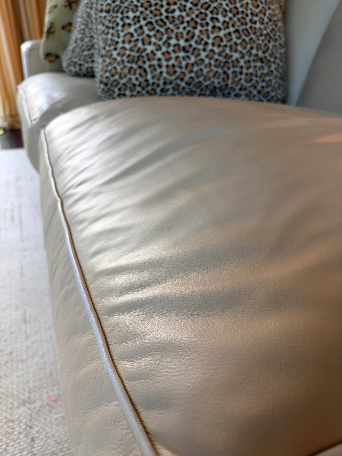 Close-up of restored leather sofa cushion edge — white contrast piping preserved and clearly defined against the custom color-matched leather surface