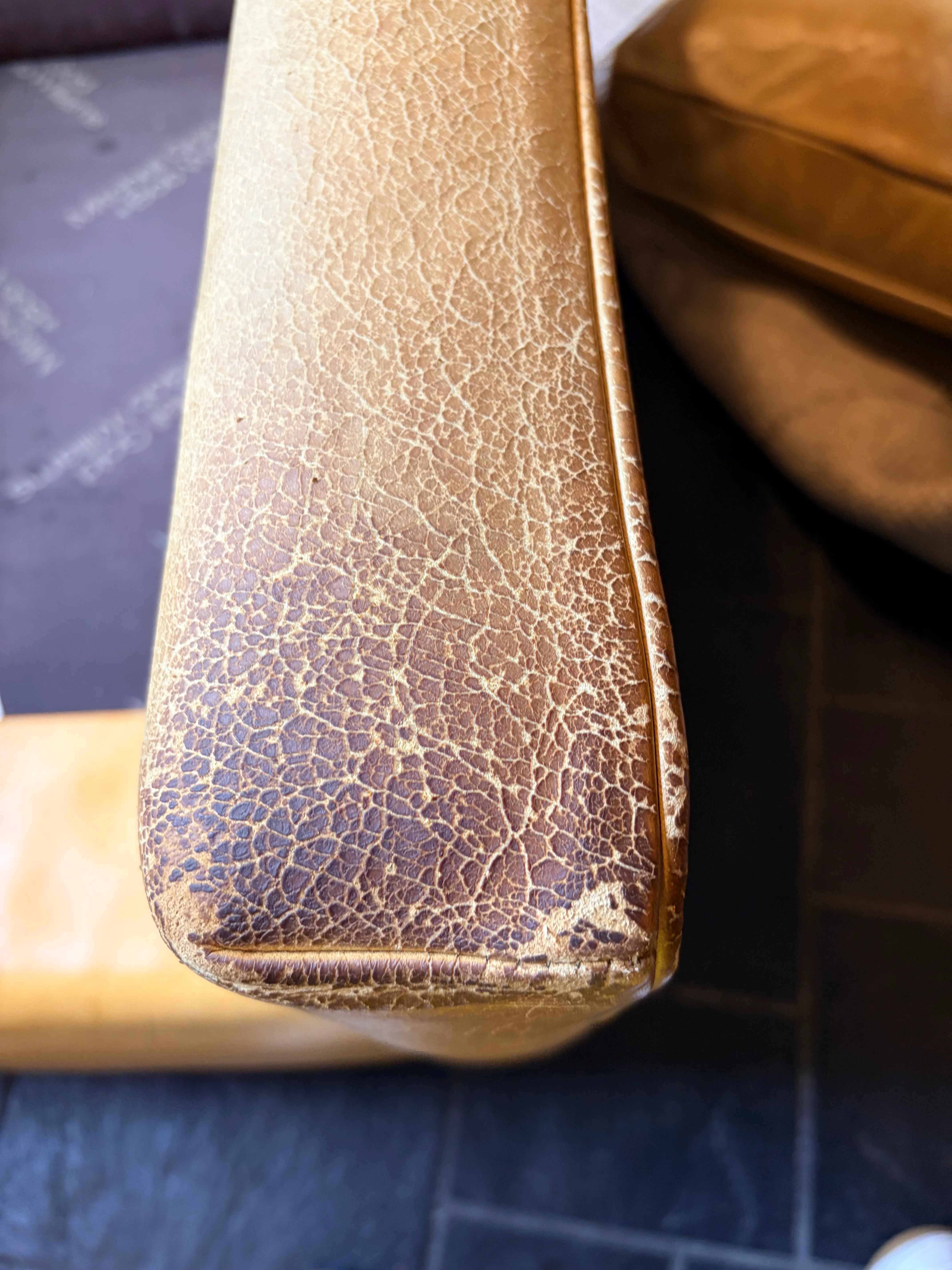 Mitchell Gold Hunter leather chair armrest corner before restoration — severe mosaic cracking, saffron color completely absent, dark substrate exposed