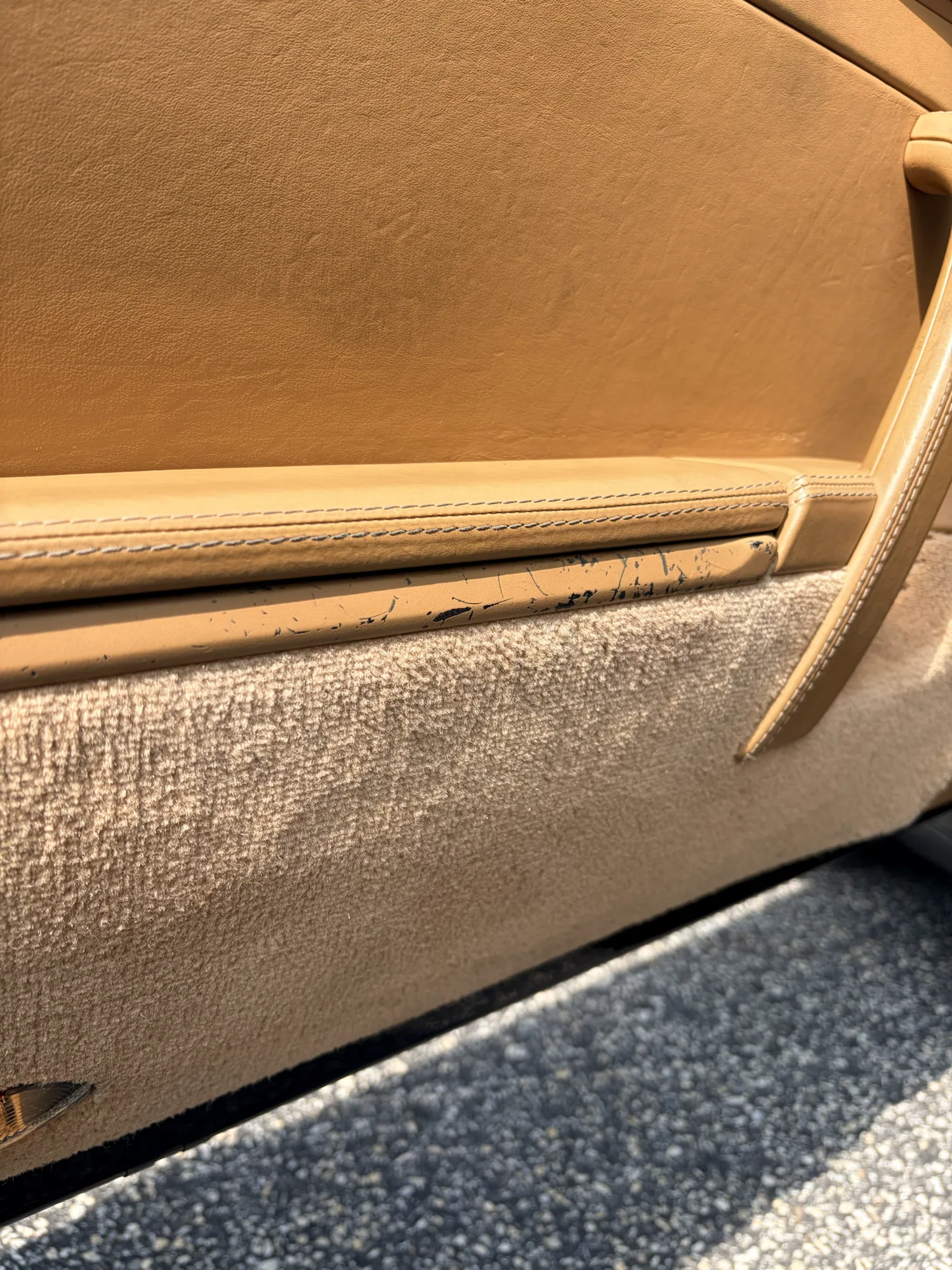 Black scratches and finish loss along the lower tan leather door trim before restoration