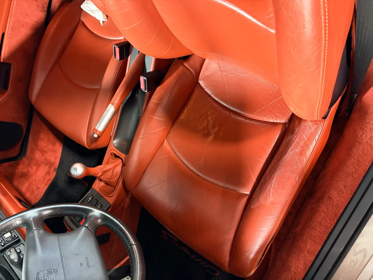 Porsche 993 Carrera S interior overview before restoration — warm terracotta leather seats showing wear and color loss across driver and passenger side