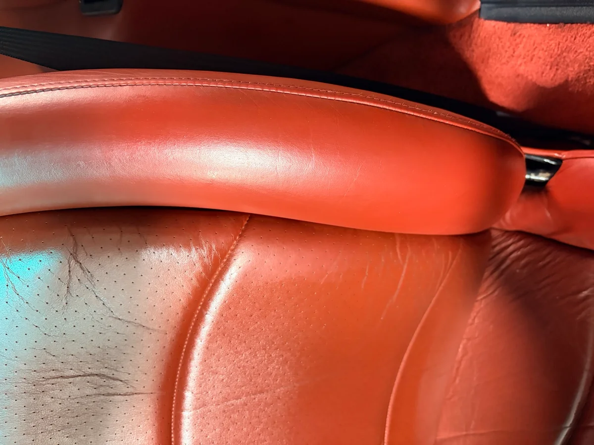 Porsche 993 driver's seat bolster after restoration — surface repaired and recolored, consistent orange-red tone, natural leather texture retained