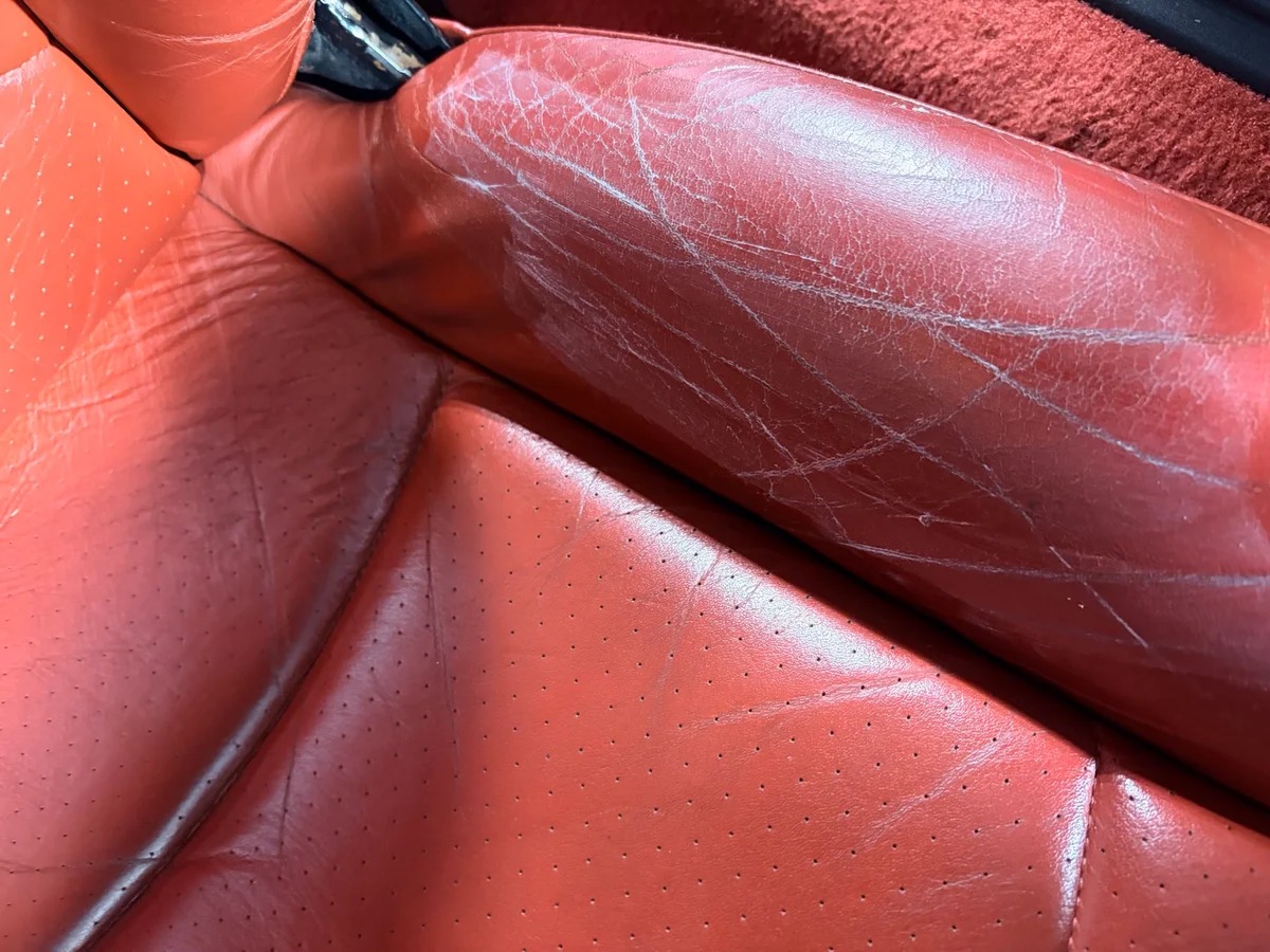 Porsche 993 lateral seat bolster before restoration — multiple surface scratches across the bolster face from driver entry and exit wear