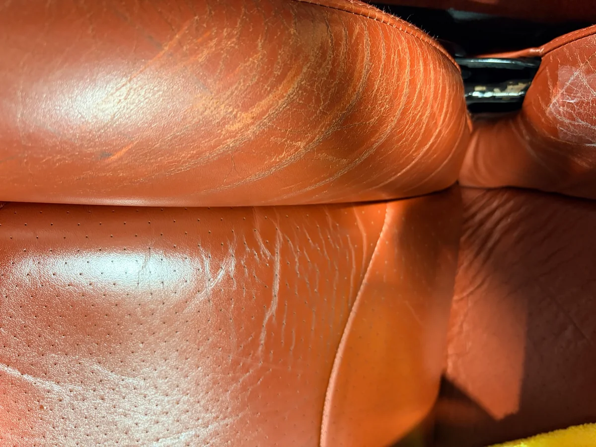 Porsche 993 driver's seat bolster before restoration — surface finish worn and discolored across the bolster top where driver contact is concentrated