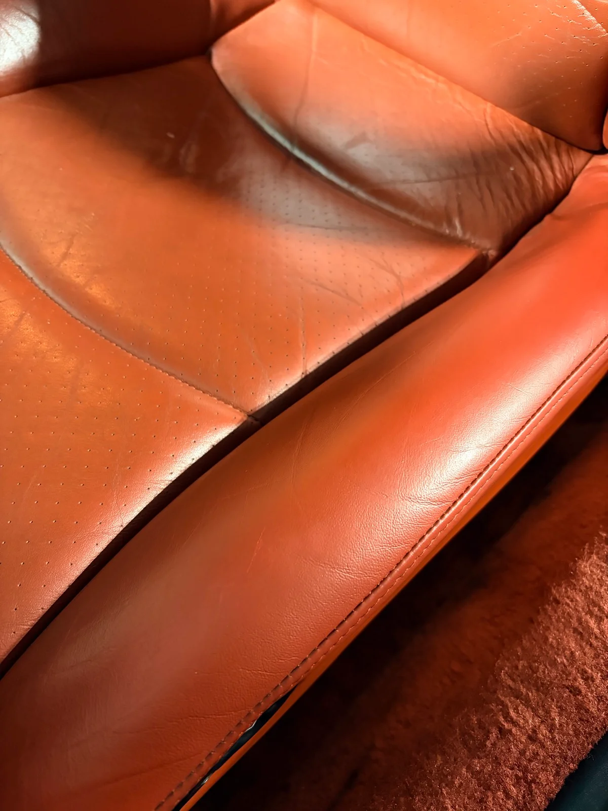 Porsche 993 perforated seat cushion and bolster after restoration — rich, even orange-red tone with natural leather creasing intact