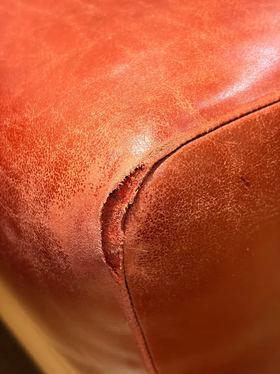 Open tear in restaurant leather booth seating at the seat/side seam before repair — leather fibers exposed, Midtown Manhattan