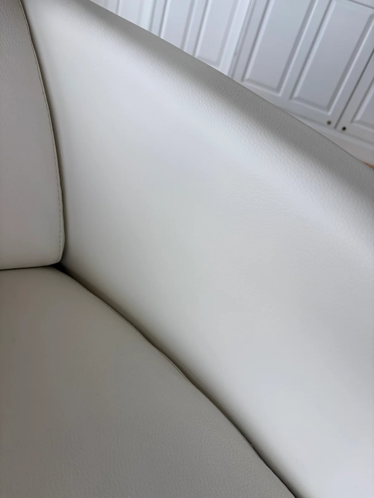 Close-up of white leather chair armrest and seat after restoration, showing preserved grain and stitching