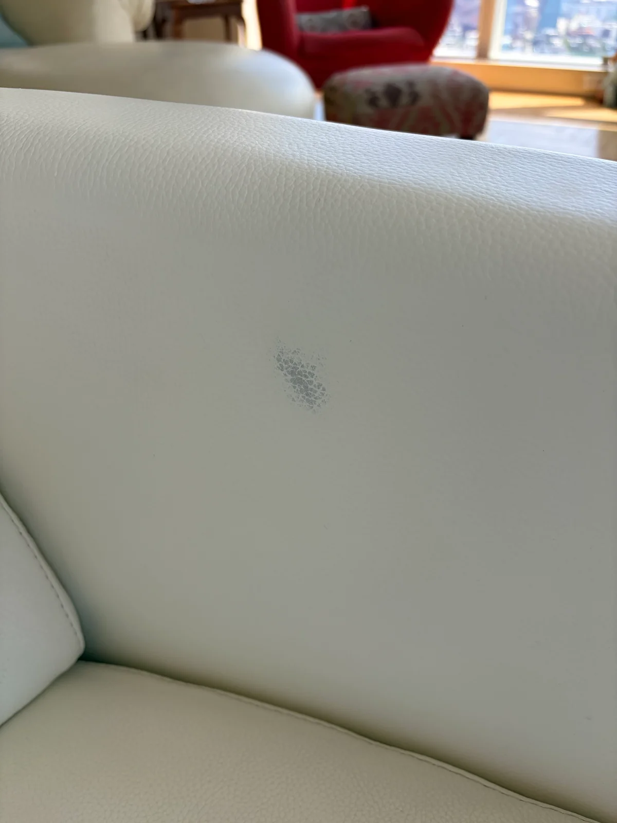 Close-up of dark hair-dye stain on the backrest of a white leather lounge chair before restoration
