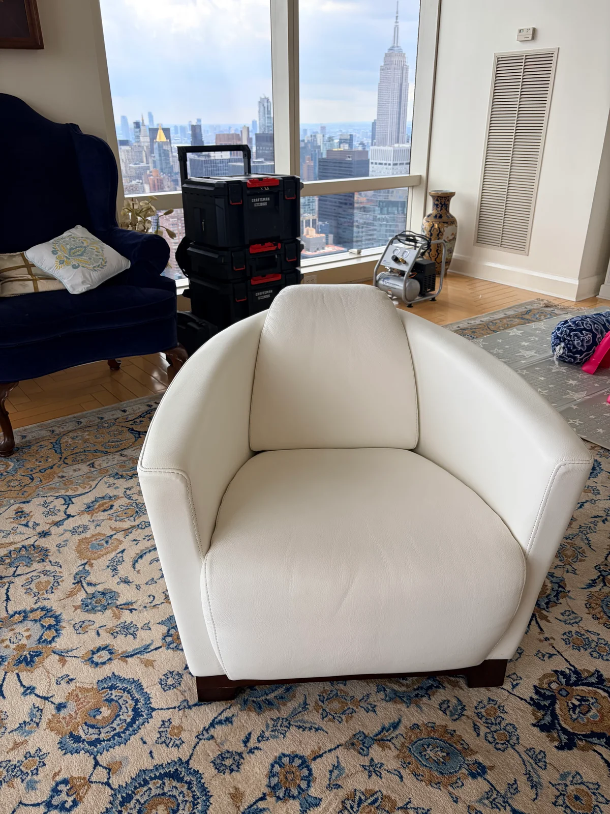 White leather lounge chair after restoration, full view in a Manhattan residence with city skyline in the background